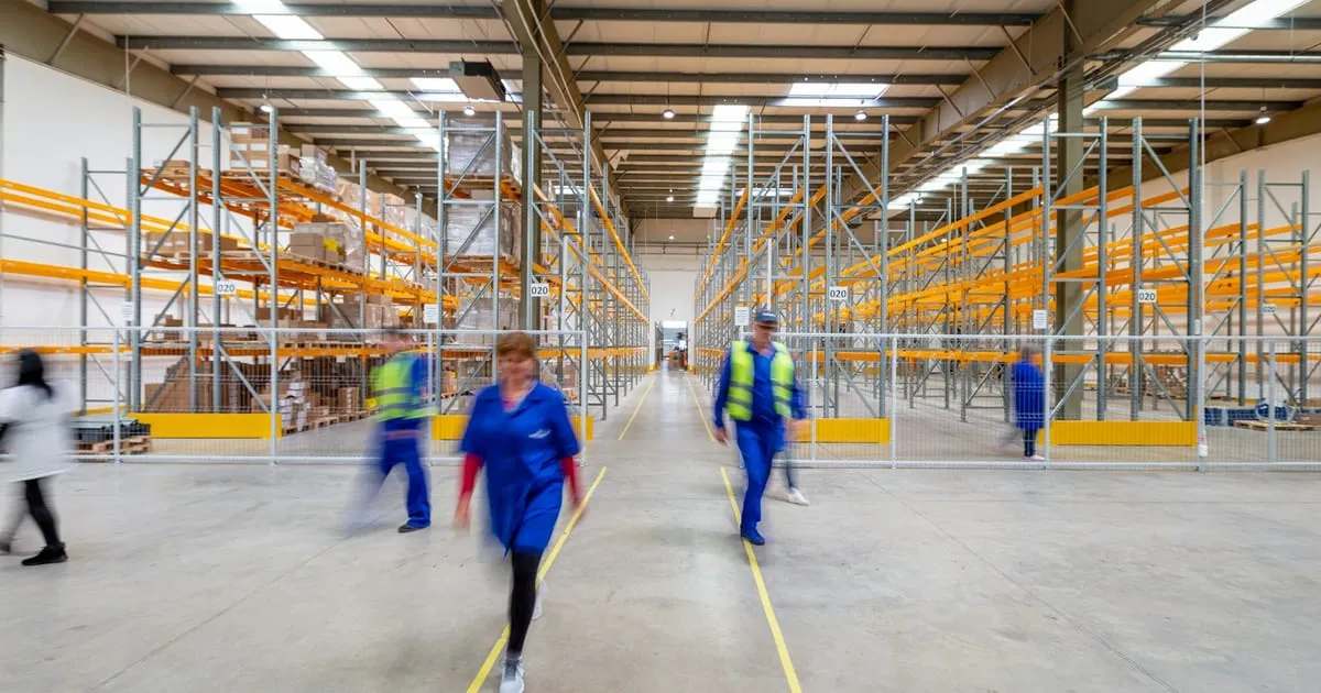 Pasillos de un almacén con estantería industrial y personal trabajando al fondo