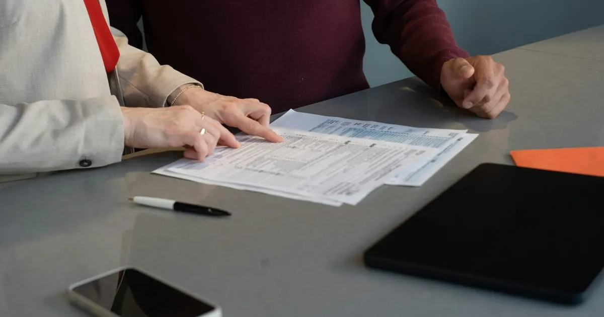Dos personas revisando un formato en papel sobre un escritorio, con un celular al lado