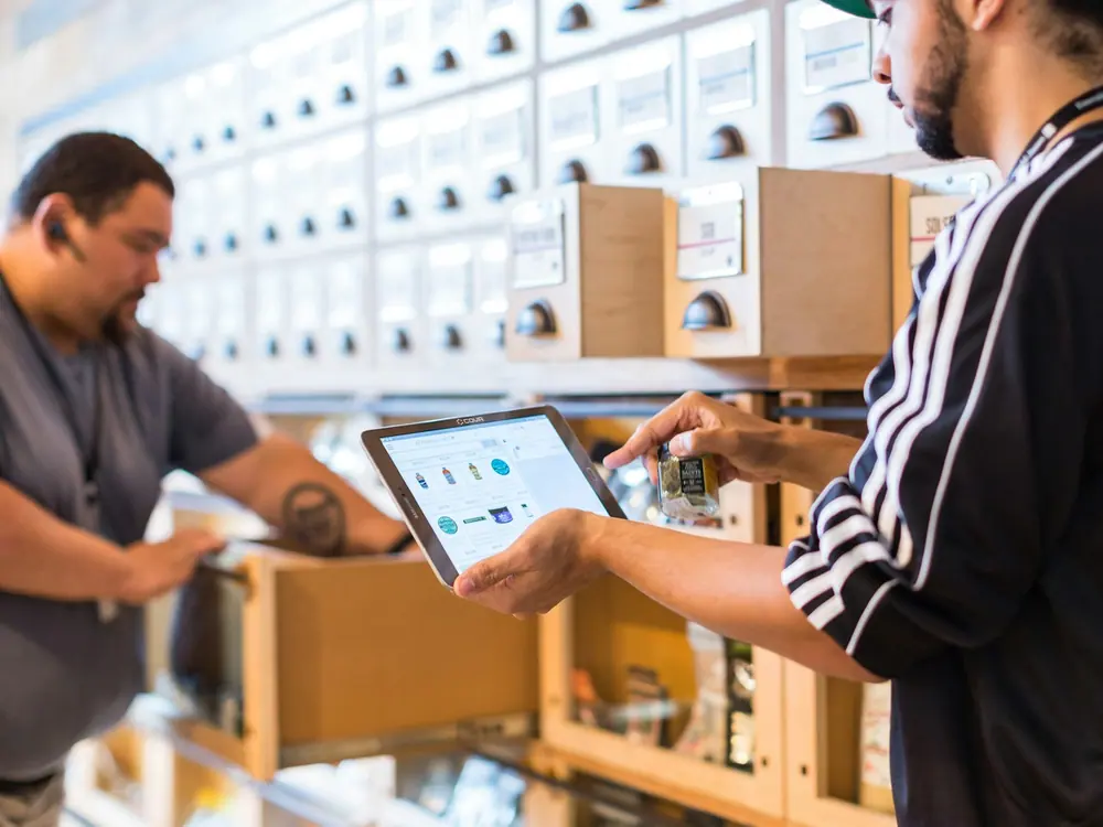 Dos trabajadores consultando el inventario en una tableta frente a la estantería de un almacén